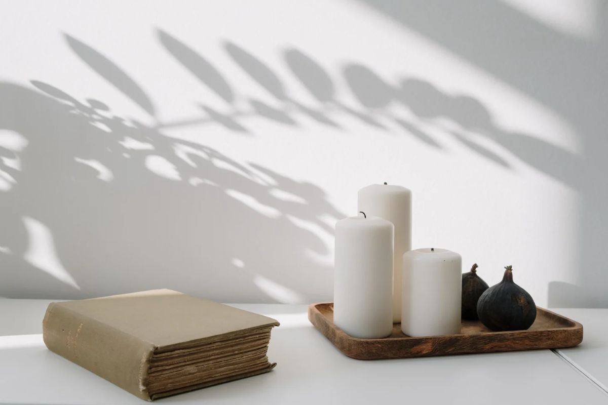 White candles on a decorative wooden tray next to a book