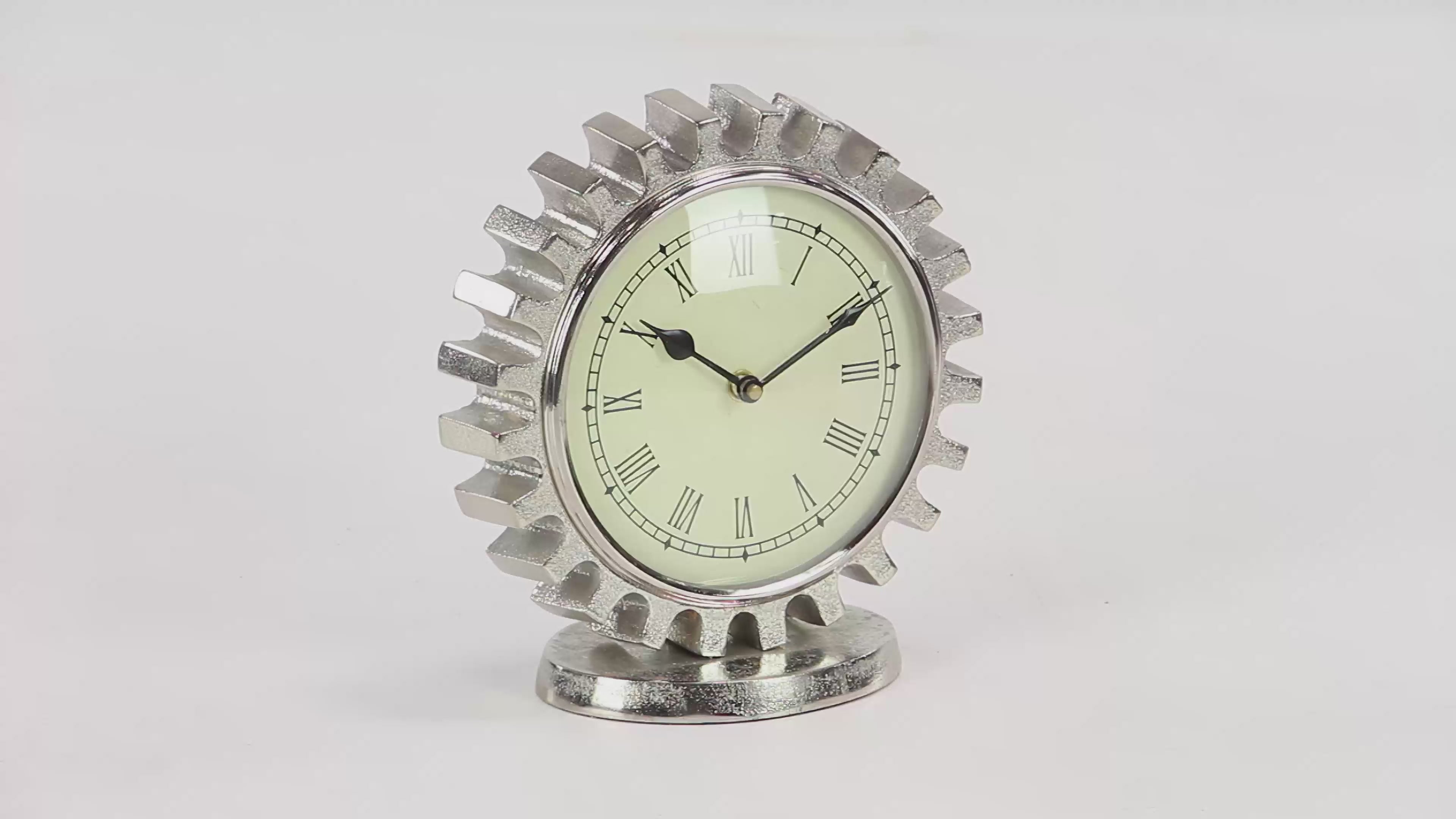 Textured silver aluminum gear shaped table clock. Clock is spinning 360 degrees and has a beige face with black roman numerals and hands. Behind is white background