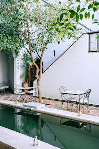 Exterior of modern building and cobblestone yard with decorative pool and tangerine tree over tables with chairs