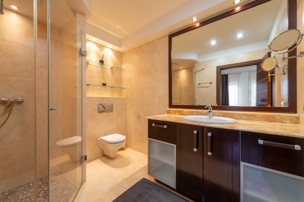 Shower room against toilet bowl and cabinet with washbasin under mirrors illuminated by shiny lamps in modern house