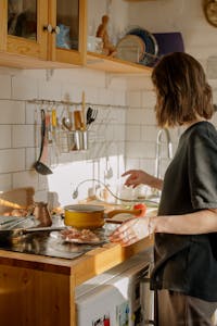 Woman in Gray Long Sleeve Shirt Standing in Front of Kitchen Sink