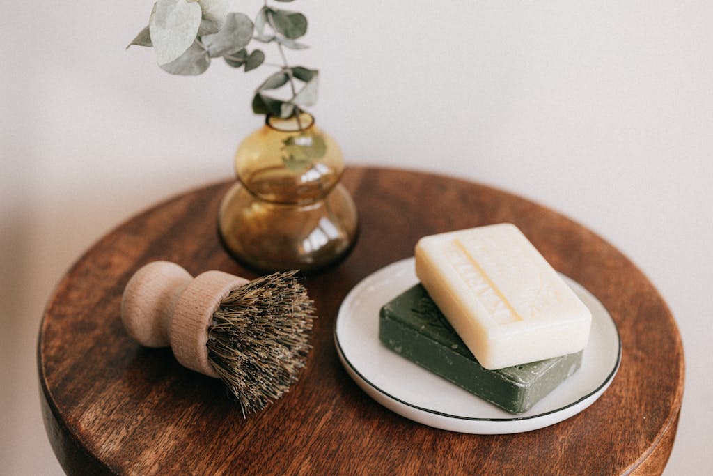 From above of handmade soaps and natural brush on wooden table composed with glass vase decorated with Eucalyptus leaf rustic decor ideas