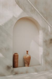 Two vases sit on a shelf in front of a window