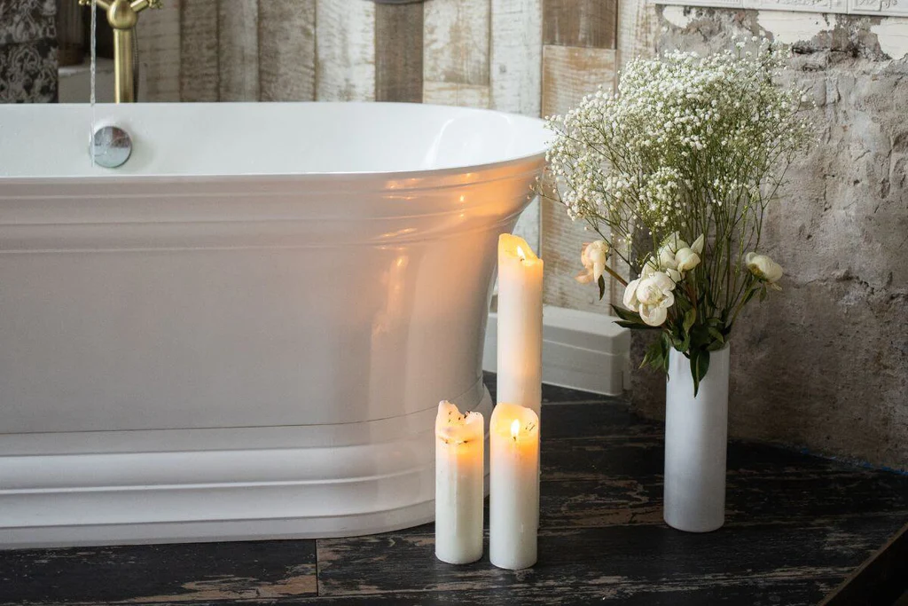 Three white candles next to a white bathtub